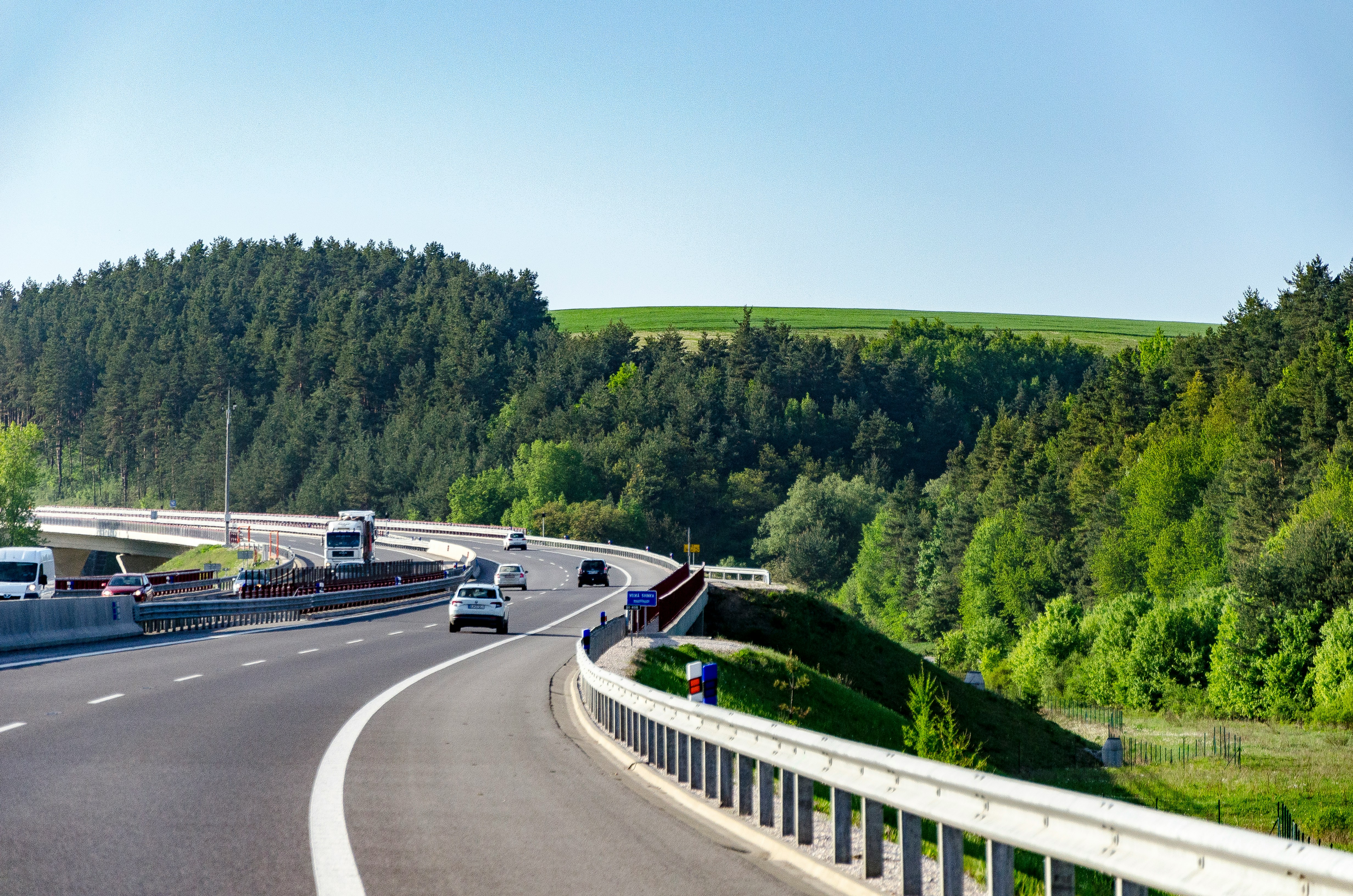 Cars driving along a European motorway, winding through green countryside under a clear sky